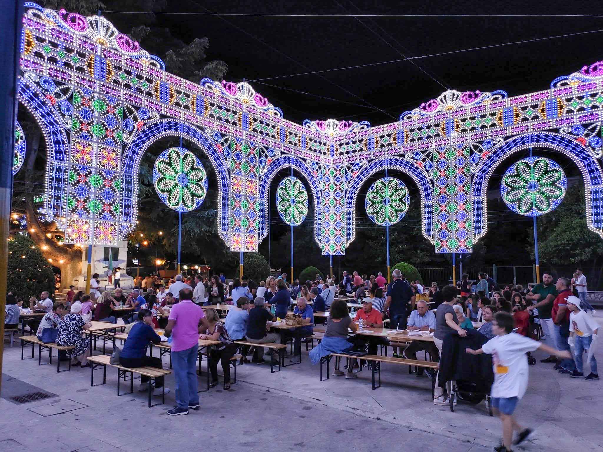 Veduta panoramica della piazza illuminata a festa con i tavoli della Sagra di Venticano